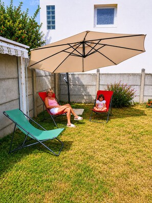 A patio with two red chairs and a green lounge chair under a large umbrella. - A vacation lulled by the sound of the sea! (Jard-sur-Mer)