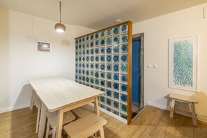 Ein Zimmer mit einem Holzesstisch, Bänken, einem an der Wand befestigten Glasbild und einer Tür mit blauem Rahmen.