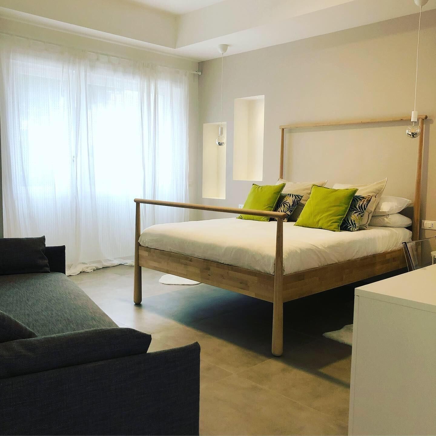 Un dormitorio moderno con estructura de cama de madera, una mesita de noche y un sofá.