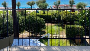 Un balcon avec vue sur la mer, un arbre et, au loin, un terrain de jeux.