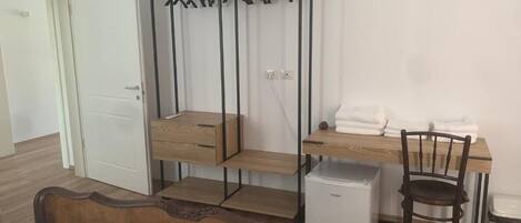 A bedroom with a bunk bed, a desk with a chair, a small refrigerator, and a bedside table.
