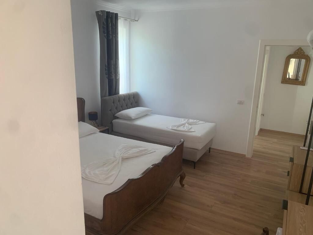 A bedroom with two single beds, a wooden floor, a window with curtains, and a door with a mirror.