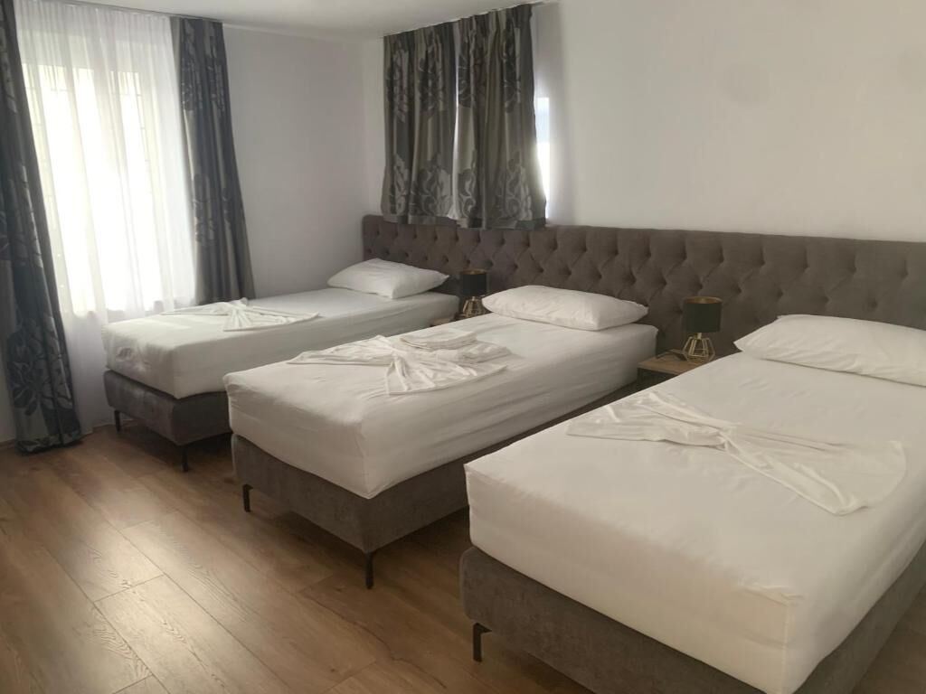 Una habitación de hotel con tres camas individuales, un cabecero grande y capitonado, y suelo de madera.