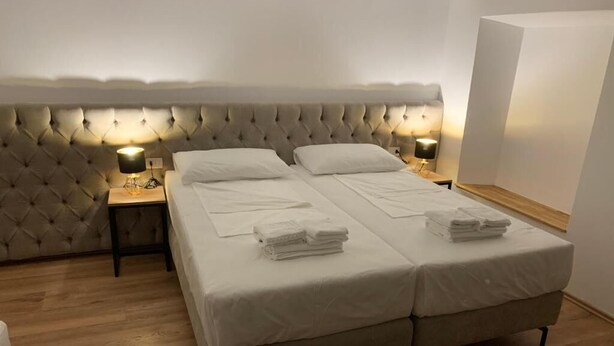 A double bed with a tufted headboard, two bedside tables with lamps, and neatly folded towels on the bed. - Vintage  (Shkoder)