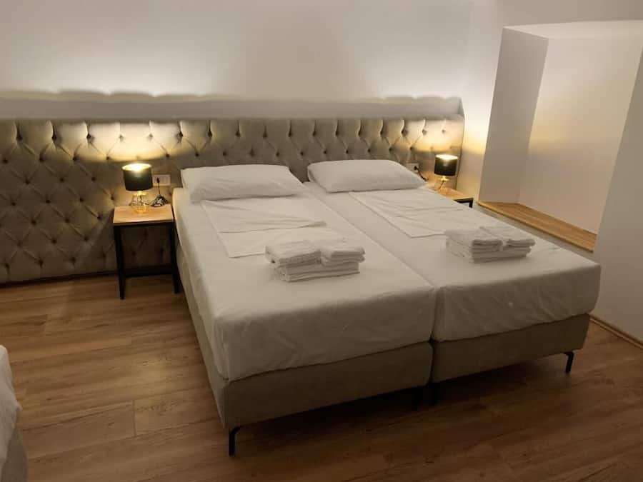 Una cama doble con cabecera capitonada, dos mesitas de noche con lámparas y toallas dobladas con esmero sobre la cama.