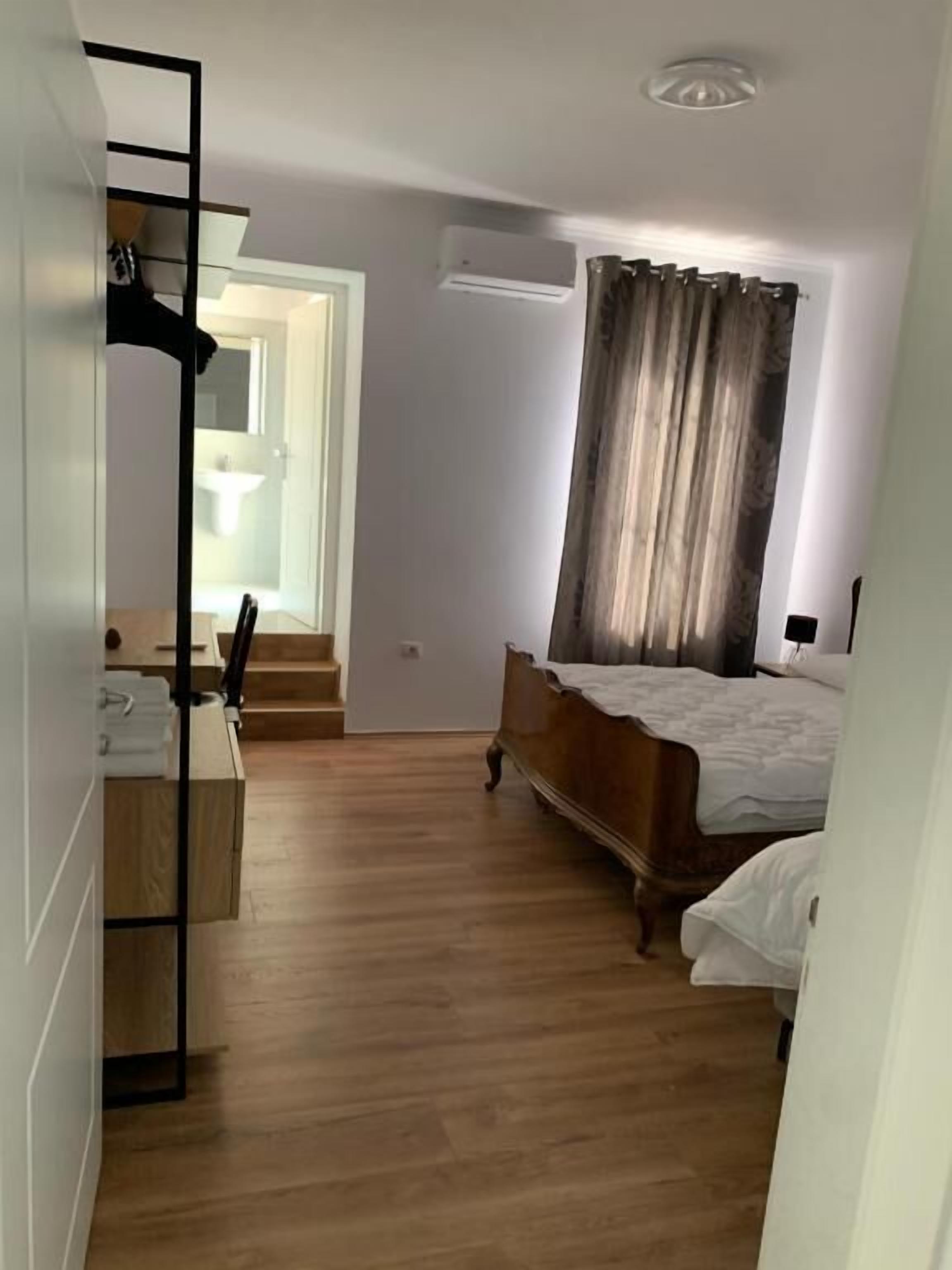 A bedroom with a wooden floor, a bed, a desk with a chair, and a wardrobe.