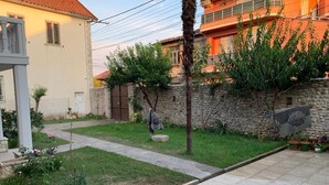 A residential area with a paved pathway, a stone wall, and a small garden with various plants. - Vintage  (Shkoder)