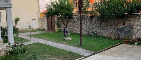 A residential area with a paved pathway, a stone wall, and a small garden with various plants.
