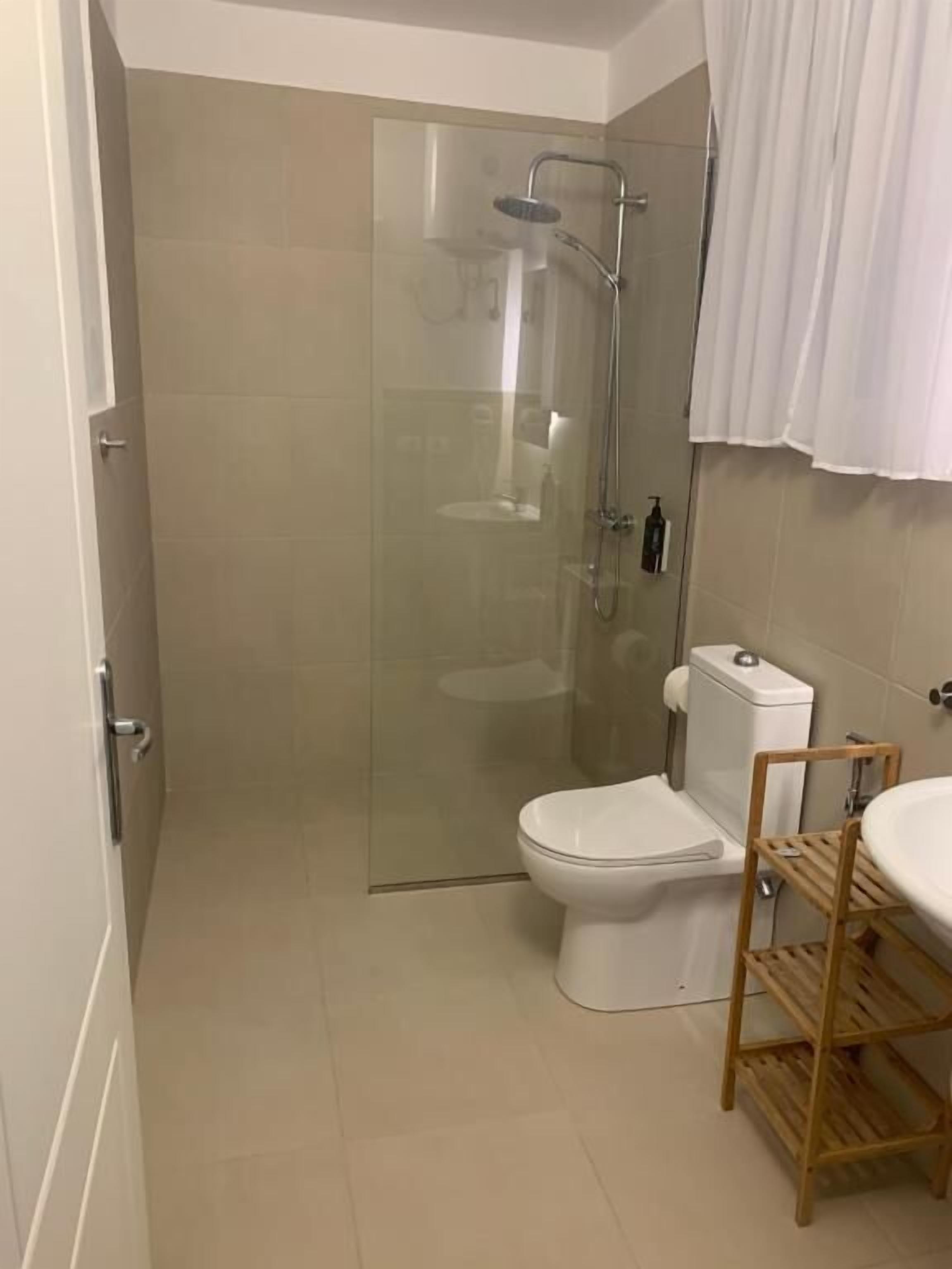 Une salle de bain avec une douche à parois de verre, des toilettes blanches et une étagère en bois.