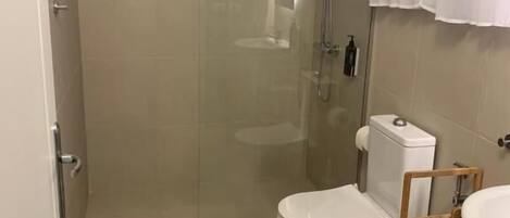 A bathroom with a glass-enclosed shower, a white toilet, and a wooden shelf.