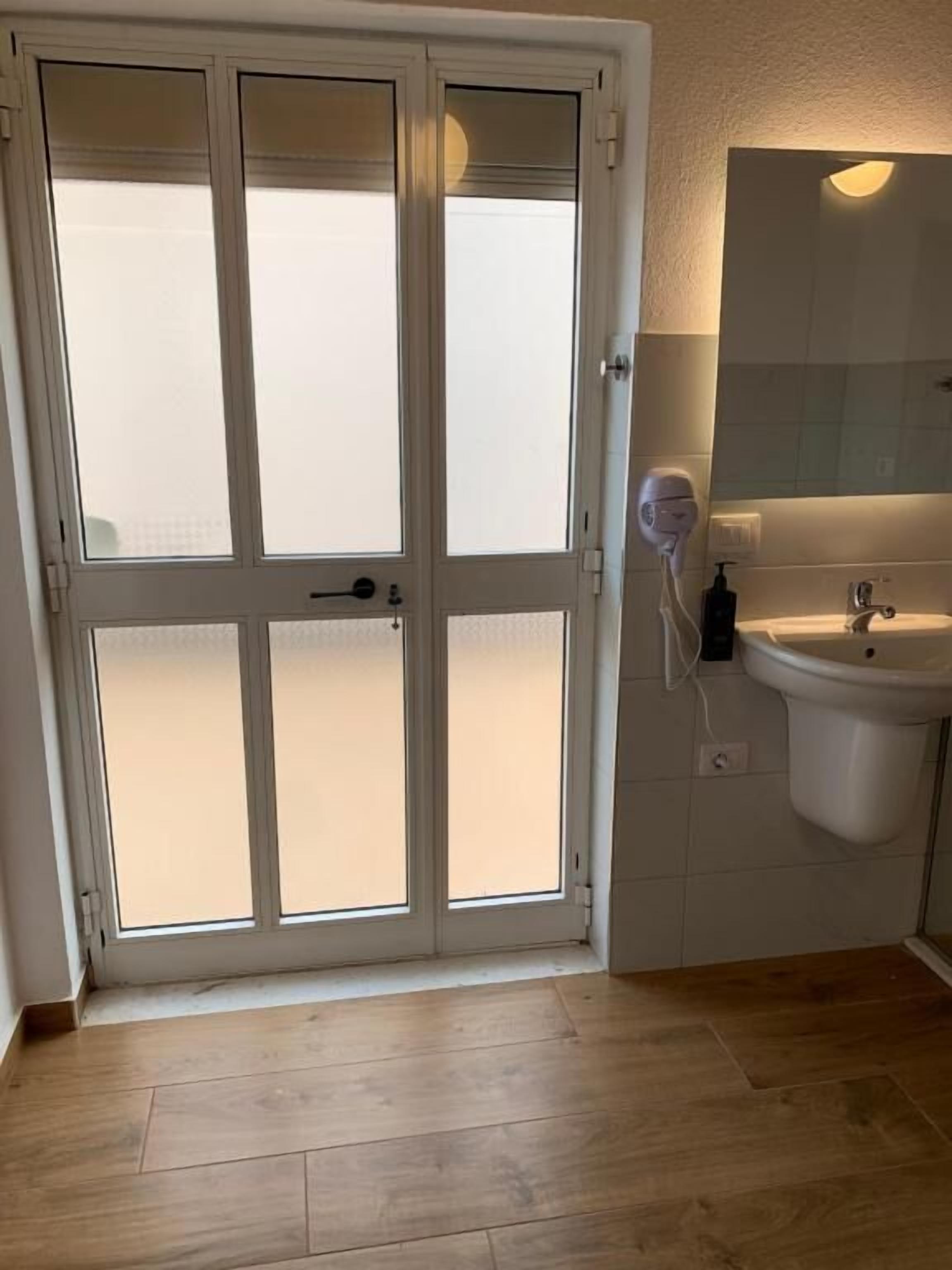 Quarto com porta de vidro fosco, pia branca e espelho acima.