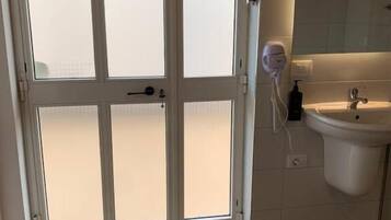 Quarto com porta de vidro fosco, pia branca e espelho acima.
