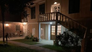 A two-story house with a staircase leading to the upper floor, a front door, and a small garden area with a pathway. - Vintage  (Shkoder)