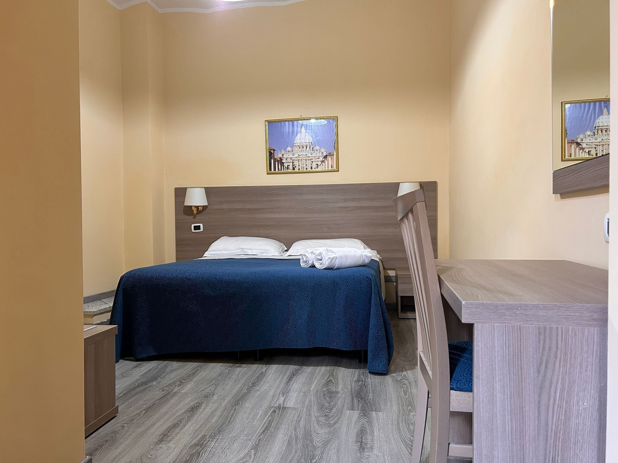 A hotel room with a bed, a desk, and a wall-mounted lamp.