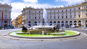 A historic fountain with multiple statues in the center, surrounded by a circular plaza with cobblestone pavement. - Accommodation Corallo (Rome)