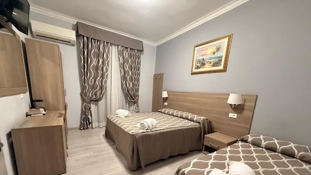 A hotel room with two beds, a desk, a TV, and a painting on the wall. - Accommodation Corallo (Rome)