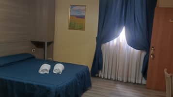 A hotel room with a bed, a wooden wardrobe, a painting on the wall, and a window with curtains.