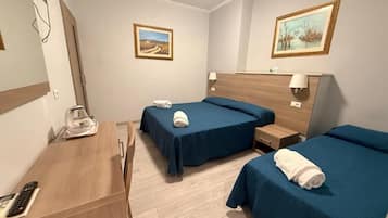 A hotel room with two single beds, a wooden desk with a telephone, and a mirror.