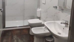 A modern bathroom with a glass-enclosed shower, a toilet, a bidet, a sink, and a mirror. - Accommodation Corallo (Rome)