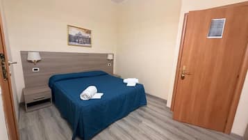 A hotel room with a bed, a nightstand, a lamp, a door, and a framed picture on the wall.