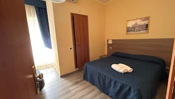A hotel room with a bed, a door, a painting, and an air conditioning unit.