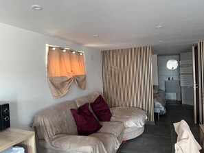 Een moderne woonkamer met een gebogen bank, een houten scheidingswand, een ronde spiegel en een inbouwwastafel.