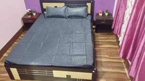 Een bed met een blauwe matras en hoofdbord, twee nachtkastjes met decoratieve voorwerpen, een houten vloer en een paarse wand.