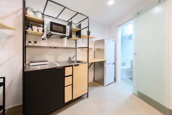 Eine moderne Küche mit eingebauter Mikrowelle, Spüle und Kühlschrank. Darüber befinden sich Holzregale und auf einem der Regale steht eine kleine Pflanze.