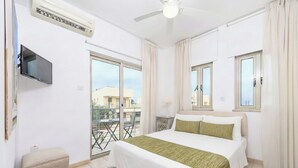 A hotel room with a bed, a television, an air conditioning unit, and a balcony with a table and chairs. - 4 bedroom villa by Fig tree bay beach (Protaras)