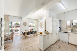 A modern kitchen with white cabinets, a dining area with a table and chairs, and a view of the outside. - 4 bedroom villa by Fig tree bay beach (Protaras)