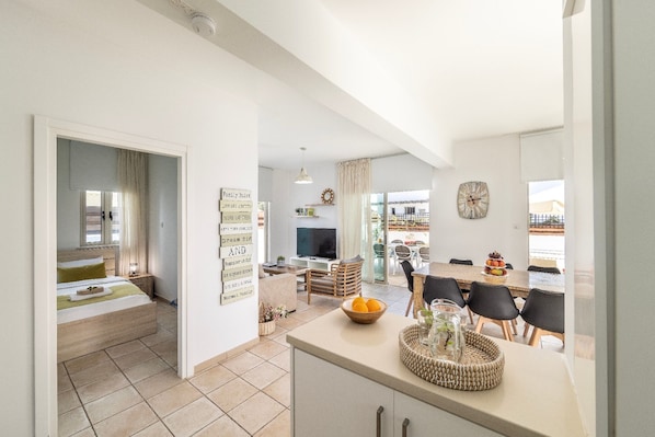 A modern living space with a kitchen, dining area, and a bedroom with a large bed and a TV. - 4 bedroom villa by Fig tree bay beach (Protaras)