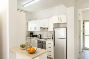 Eine moderne Küche mit weißen Schränken, Edelstahlgeräten und einer Obstschale auf der Arbeitsplatte.