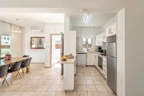 A modern kitchen with white cabinets, a stainless steel refrigerator, and a dining area with a table and chairs. - 4 bedroom villa by Fig tree bay beach (Protaras)