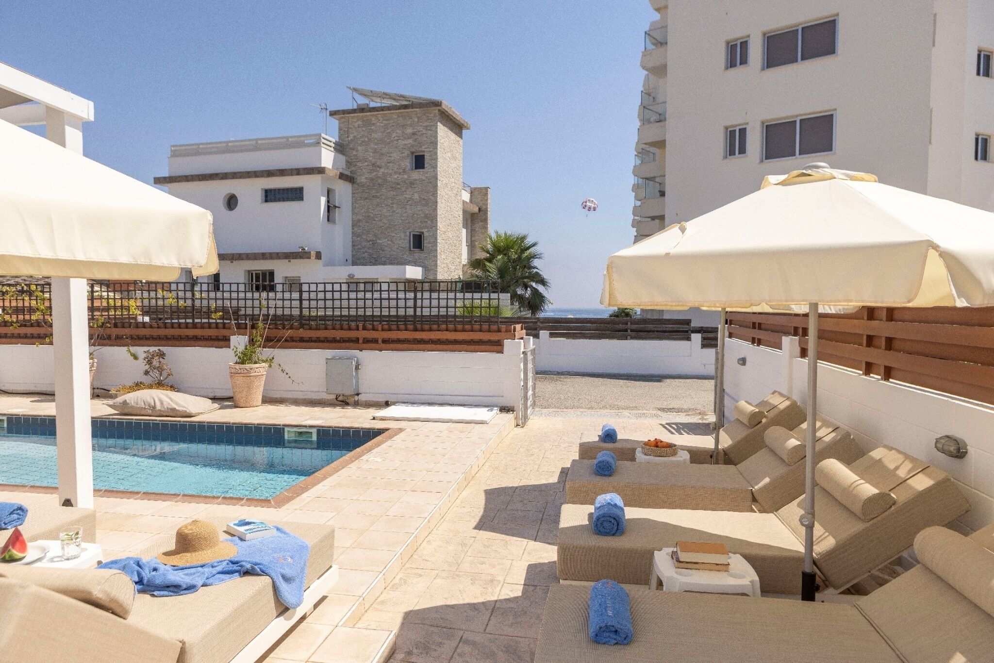 A rooftop pool area with lounge chairs and umbrellas, a clear view of the sea, and a stone building in the background.