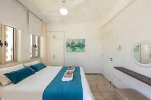 A bedroom with a bed, a ceiling fan, a window, a door, a wall-mounted artwork, and a round mirror. - 4 bedroom villa by Fig tree bay beach (Protaras)