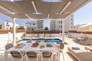 A rooftop pool area with a table set for dining, surrounded by lounge chairs and a covered seating area. - 4 bedroom villa by Fig tree bay beach (Protaras)