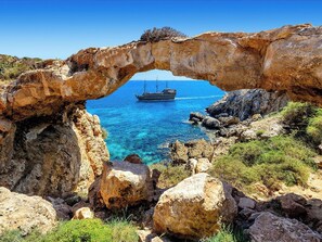 A rocky arch formation with a clear blue sea and a ship in the distance. - 4 bedroom villa by Fig tree bay beach (Protaras)