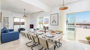 A modern living room with a dining area, large windows, and a view of the city. - 4 bedroom villa by Fig tree bay beach (Protaras)