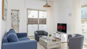 A modern living room with a sofa, armchairs, a coffee table, and a TV displaying Netflix. - 4 bedroom villa by Fig tree bay beach (Protaras)