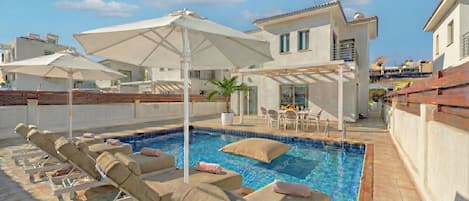 A rooftop pool area with lounge chairs, umbrellas, and a dining setup.