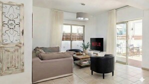 A living room with a sofa, a black armchair, a coffee table, and a TV displaying 'NETFLIX'. - 4 bedroom villa by Fig tree bay beach (Protaras)