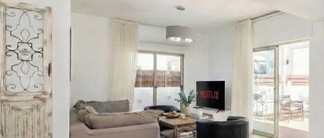 A living room with a sofa, a black armchair, a coffee table, and a TV displaying 'NETFLIX'.