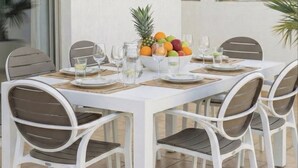 A white dining table with four chairs, a fruit bowl, and glasses on a tiled patio. - 4 bedroom villa by Fig tree bay beach (Protaras)
