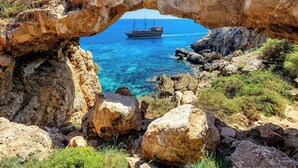 Un'imponente formazione rocciosa ad arco, con un mare cristallino e una nave all'orizzonte.