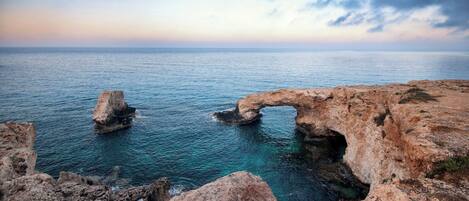 A coastal landscape with natural rock formations and a clear view of the sea.