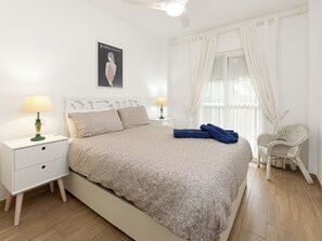 Ein ordentlich eingerichtetes Schlafzimmer mit einem Bett, zwei Nachttischen mit Lampen, einem Sessel und einem Fenster mit Vorhängen.
