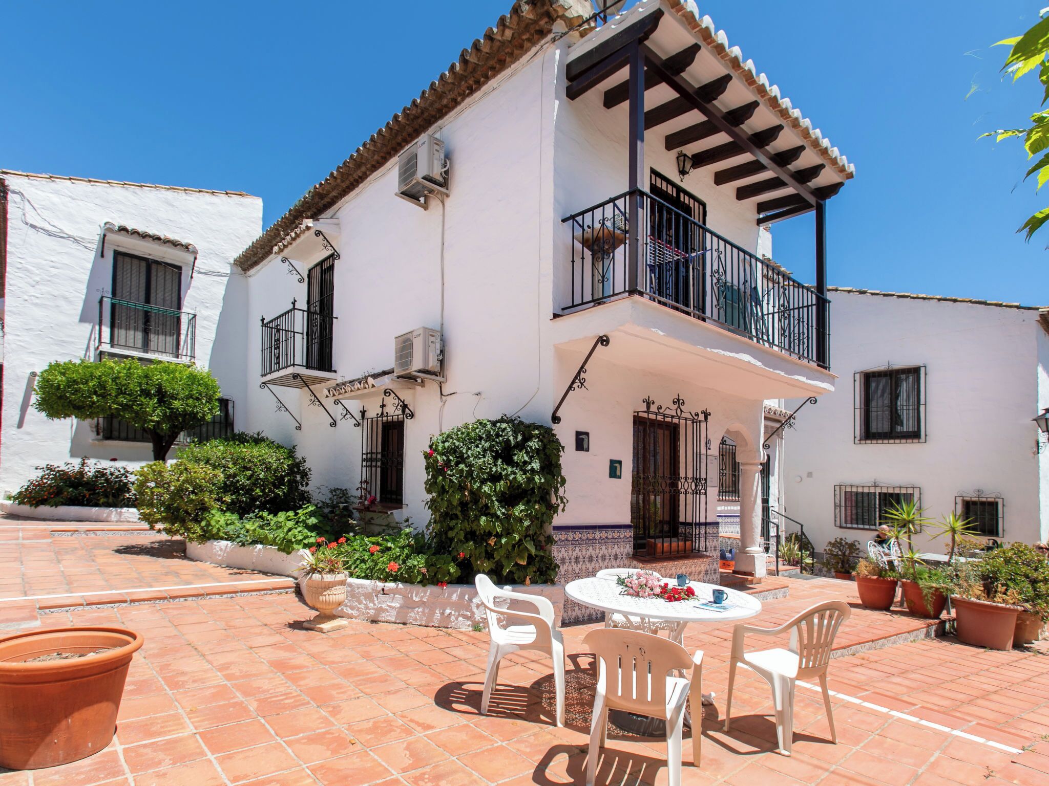 A two-story building with a balcony, terracotta tiled patio, and potted plants.
