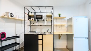Une cuisine compacte équipée d’un four à micro-ondes encastré, d’un évier et d’un réfrigérateur blanc.