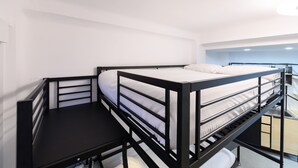 Un lit superposé avec un bureau en dessous, des murs blancs et un luminaire au plafond.