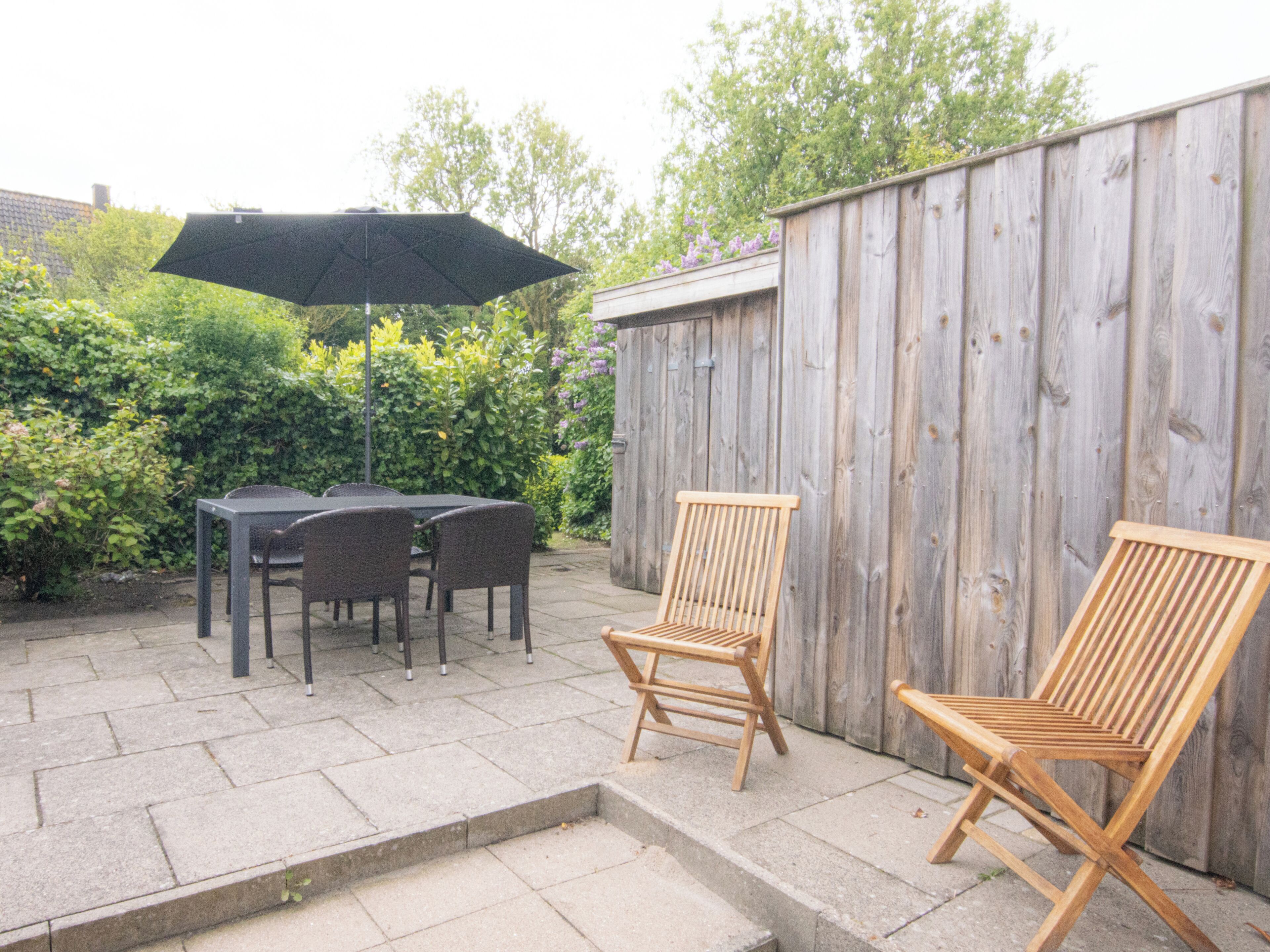 An outdoor patio with a table and chairs, a wooden fence, and a wooden chair.